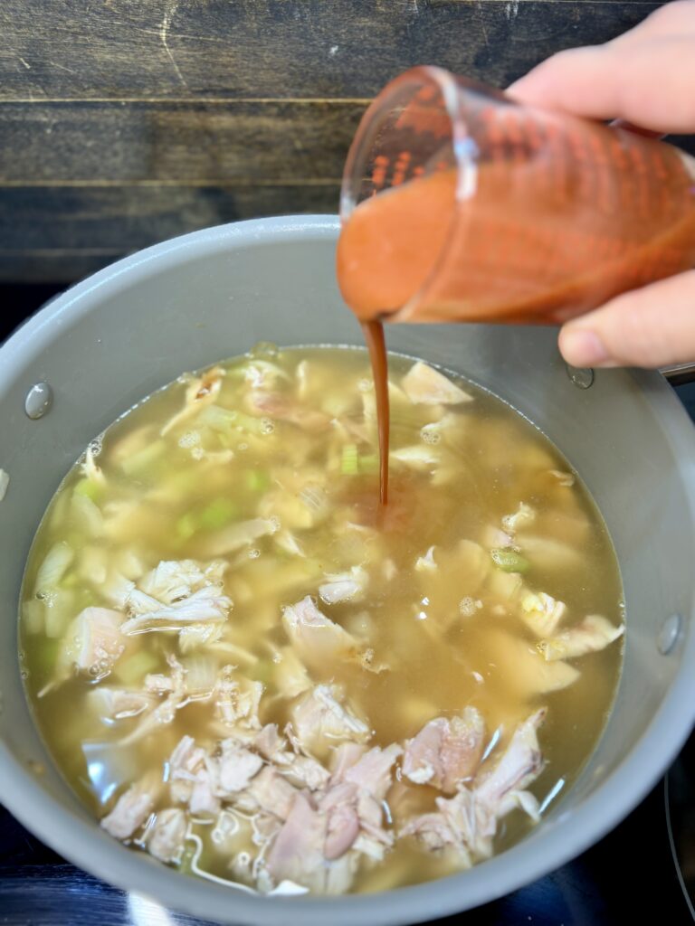 hot sauce being poured in to pot with chicken and vegetables