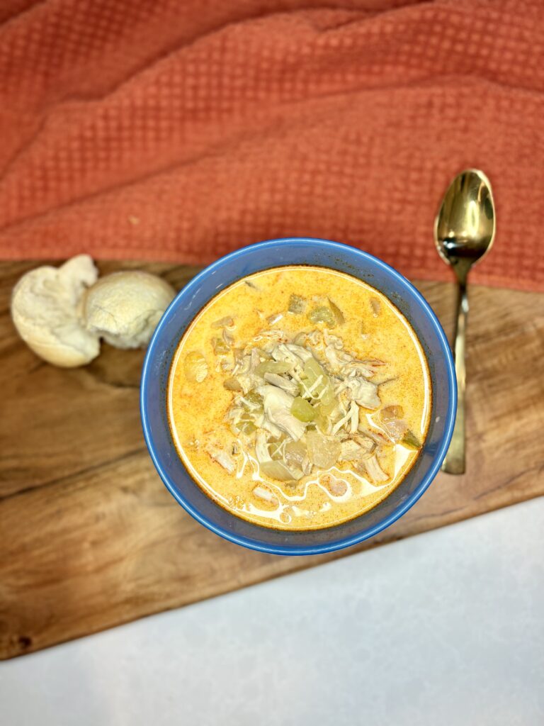 buffalo chicken soup in a bowl next to a spoon and bread on a counter 