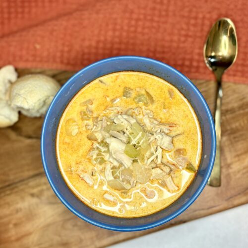 buffalo chicken soup in a bowl next to bread and a spoon on a counter