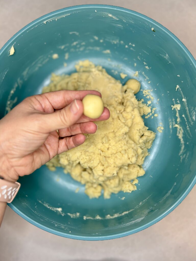 a hand showing cookie dough rolled into a 1 inch ball