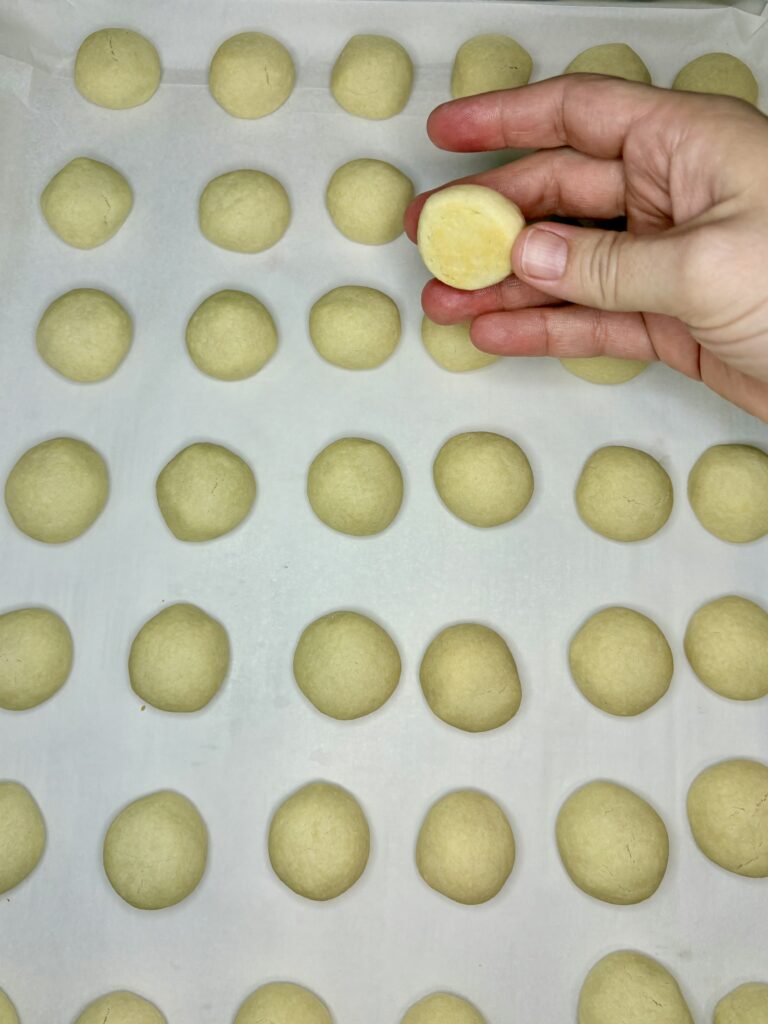 cooked russian tea cakes with a hand showing a slightly browned cookie bottom 