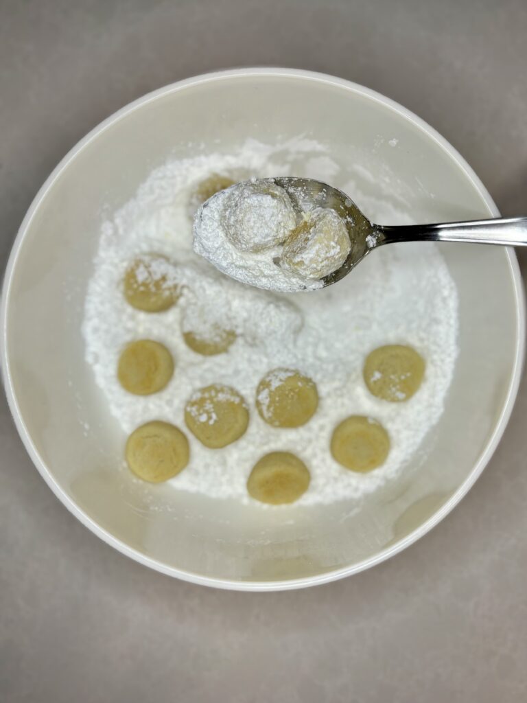 russian tea cakes on a slotted spoon in a bowl full of powdered sugar