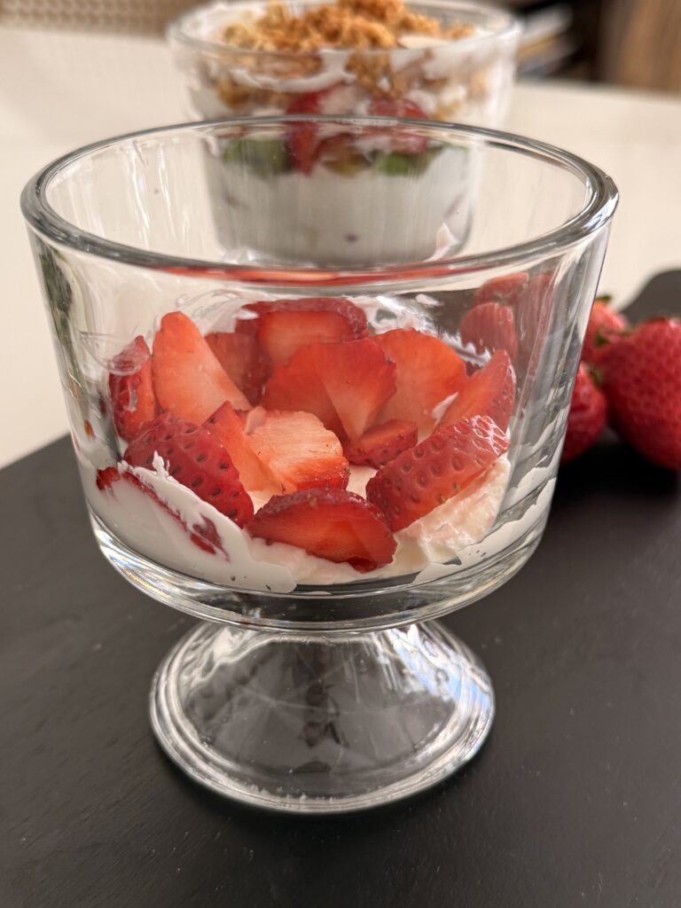 A layer of strawberries in a glass jar on a black cutting board on the counter.