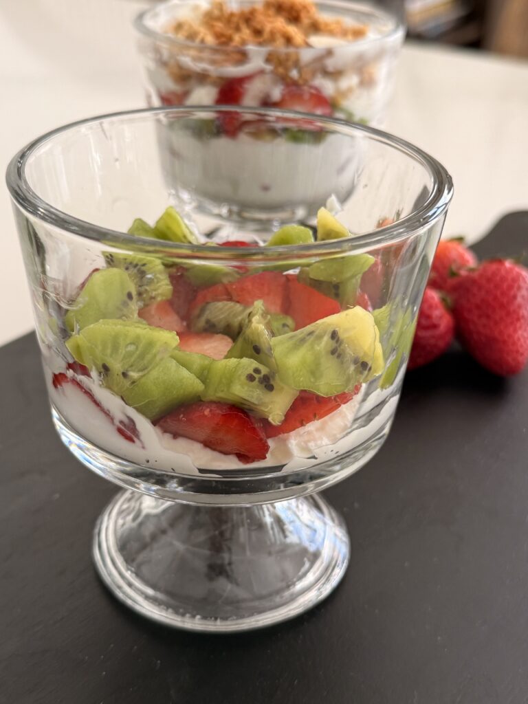 A layer of yogurt and fruit in a glass jar on a black cutting board on the counter.