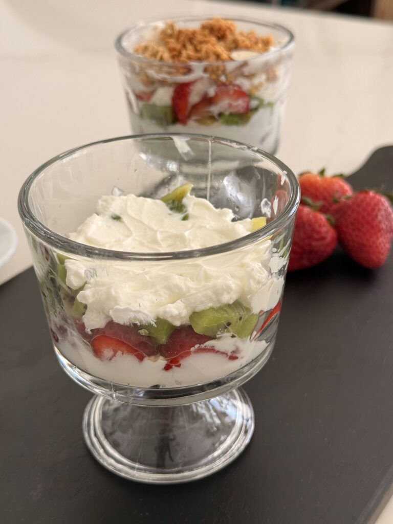 Layers of yogurt and fruit in a glass jar on a black cutting board on the counter.