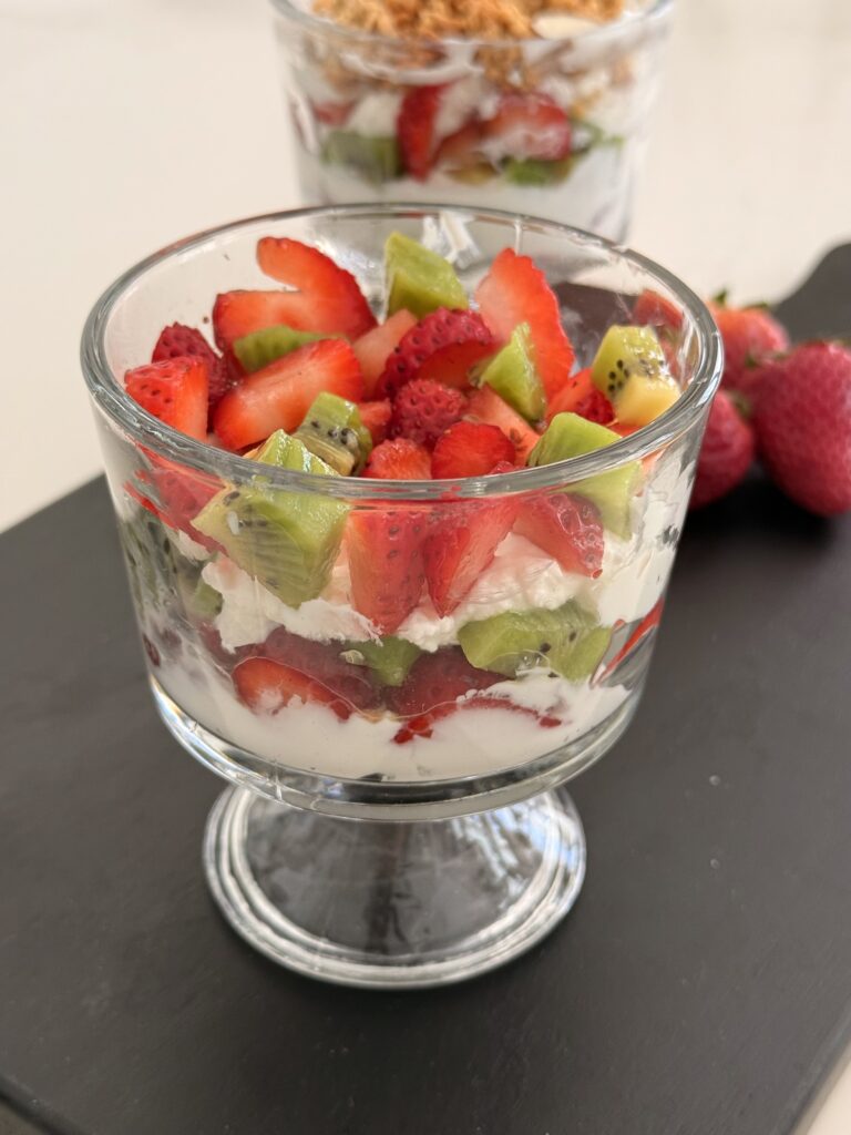 Layers of yogurt and fruit in a glass jar on a black cutting board on the counter.