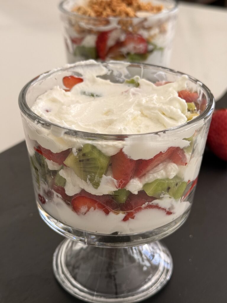 Layers of yogurt and fruit in a glass jar on a black cutting board on the counter.