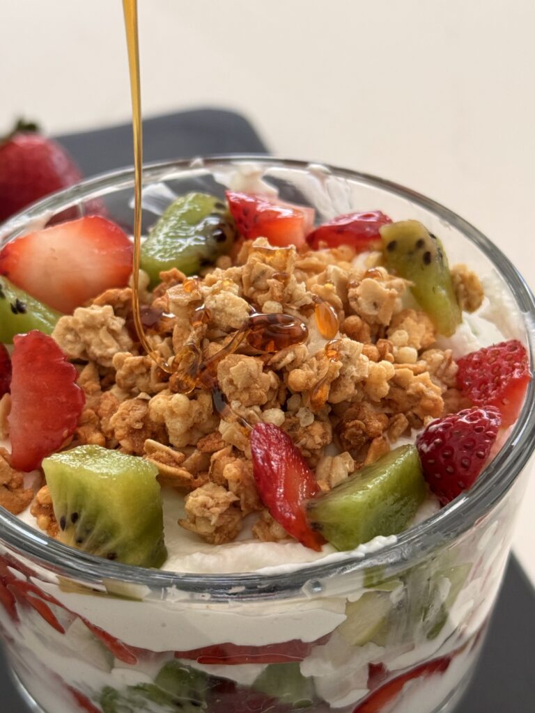 Honey being drizzled on top of the yogurt parfait in a glass on the counter.