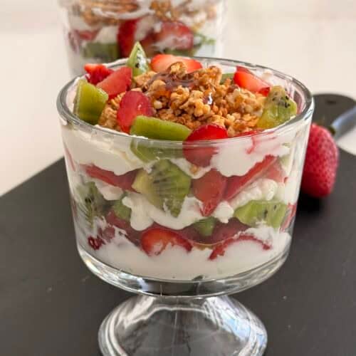 Fresh berry and granola parfait layered with whipped cream in a glass, featuring strawberries, kiwis, and granola topping for a healthy breakfast or dessert option.