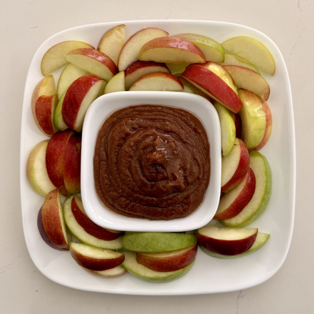 Caramel and Peanut Butter dessert dip on a white bowl on a large white plate surrounded by apples on the counter.