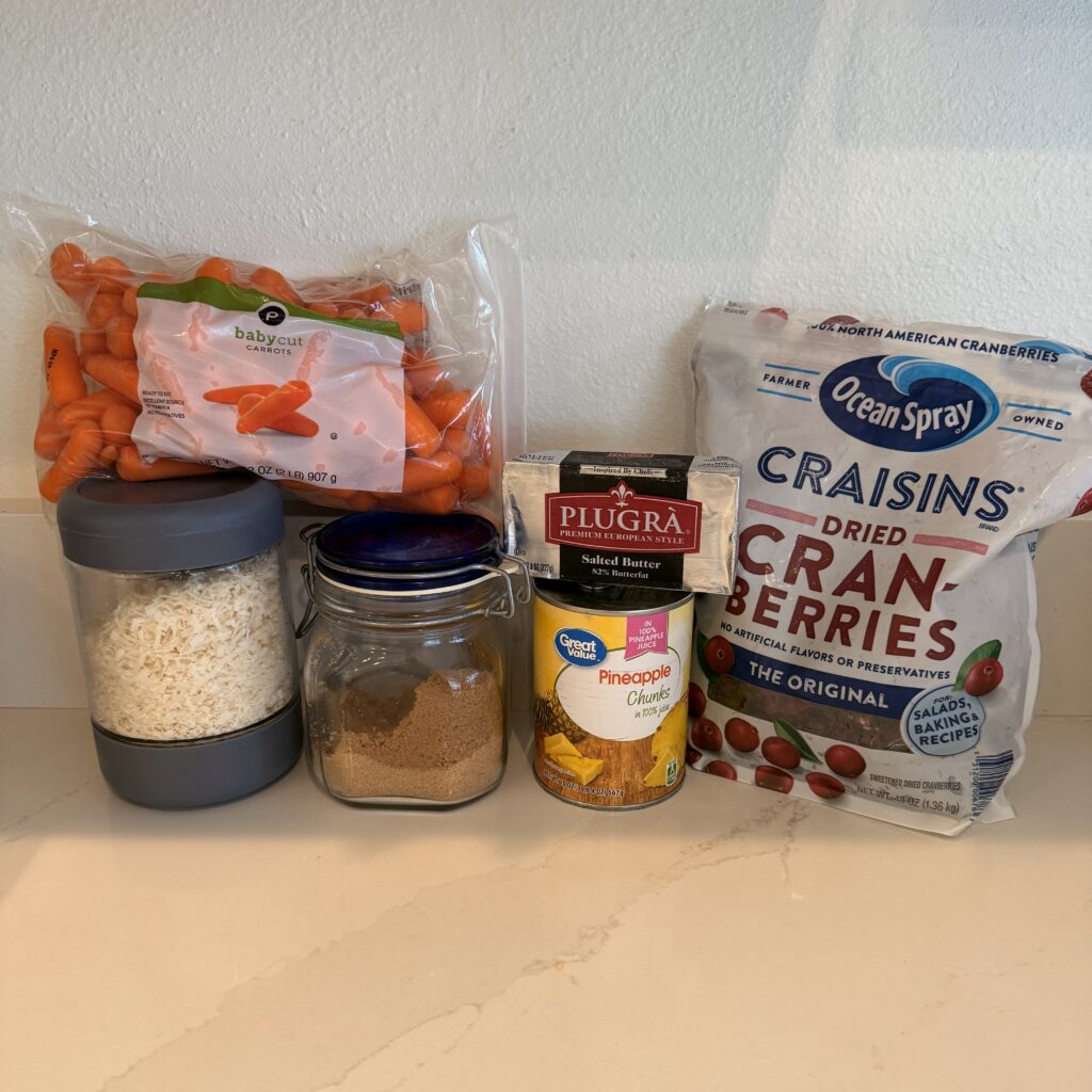 baby carrots, brown sugar, butter, canned crushed pineapple-undrained, shredded coconut, and dried cranberries on the counter.