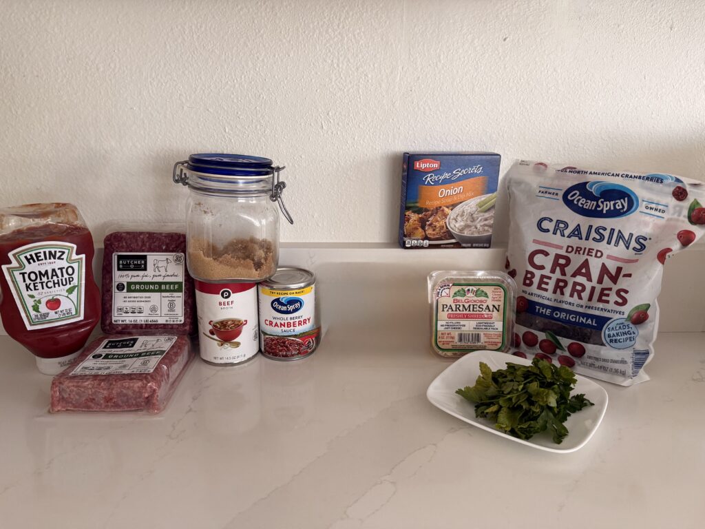 ground beef, dry onion soup mix, shredded paramasan cheese, dried cranberries, parsley, can of whole berry Cranberry sauce, ketchup, beef broth and brown sugar on the counter.