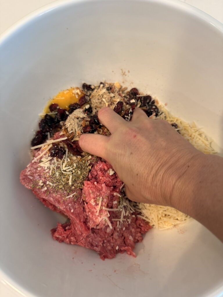 hand mixing meatloaf ingredients in a large white mixing bowl, on the counter.