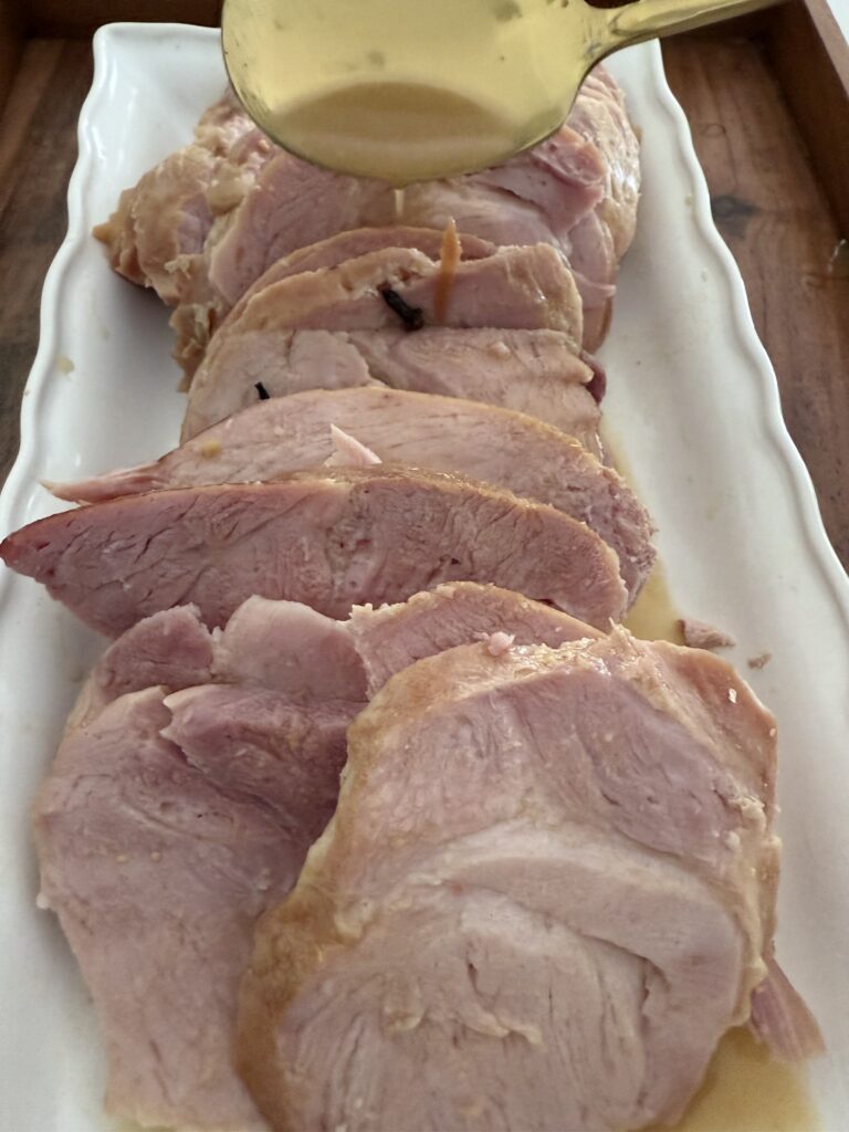 Sliced Traditional Honey Dijon Ham on a white platter on a brown tray on the counter.