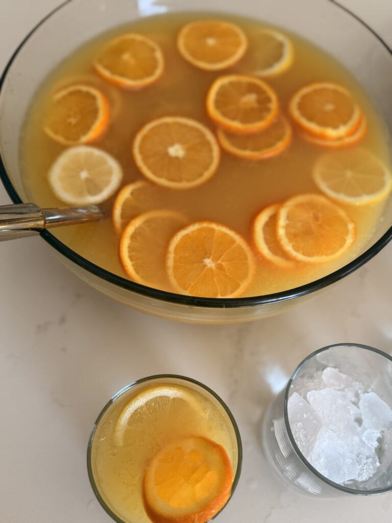 Citrus Fruit Party Punch in a punch bowl and in a punch glass on the counter.