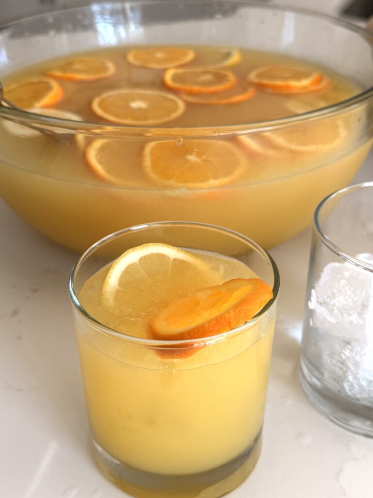 Citrus Fruit Party Punch in a large punch bowl as well as in a small glass on the counter.