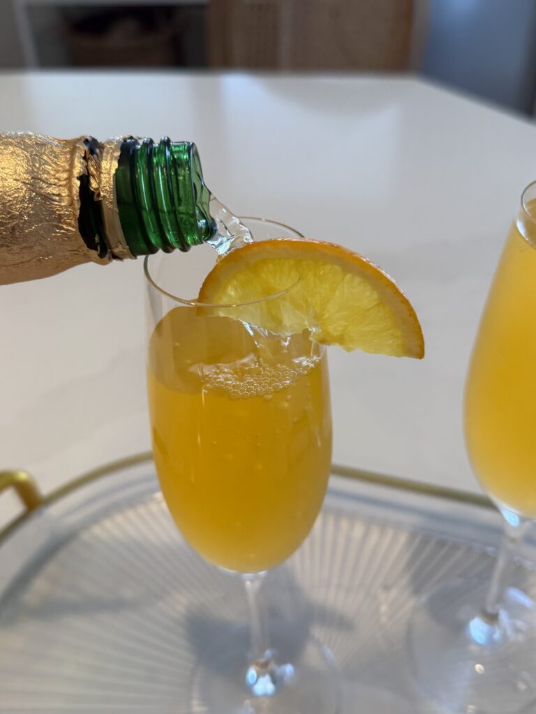 passion fruit juice with sparkling white grape juice being pouring into a champagne flute on the counter. 