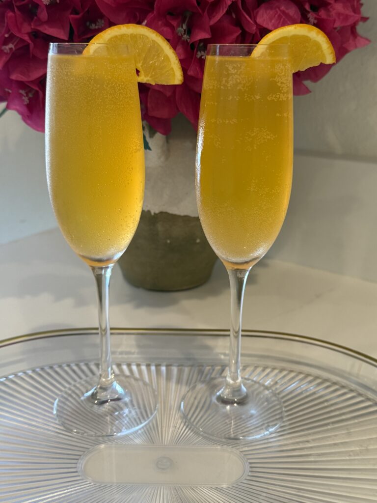 two champagne flutes filled with Fizzy Passion Fruit Refresher on a glass tray on the counter. pink flowers in a vase on the counter.