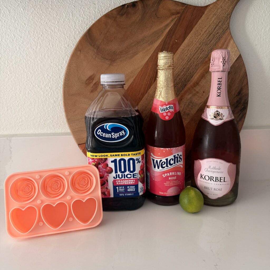 Heart shaped ice cube mold with Cran-raspberry juice, a lime, Rose Prosecco and  Sparkling Rose non-alcoholic Grape Juice Cocktail on the counter.