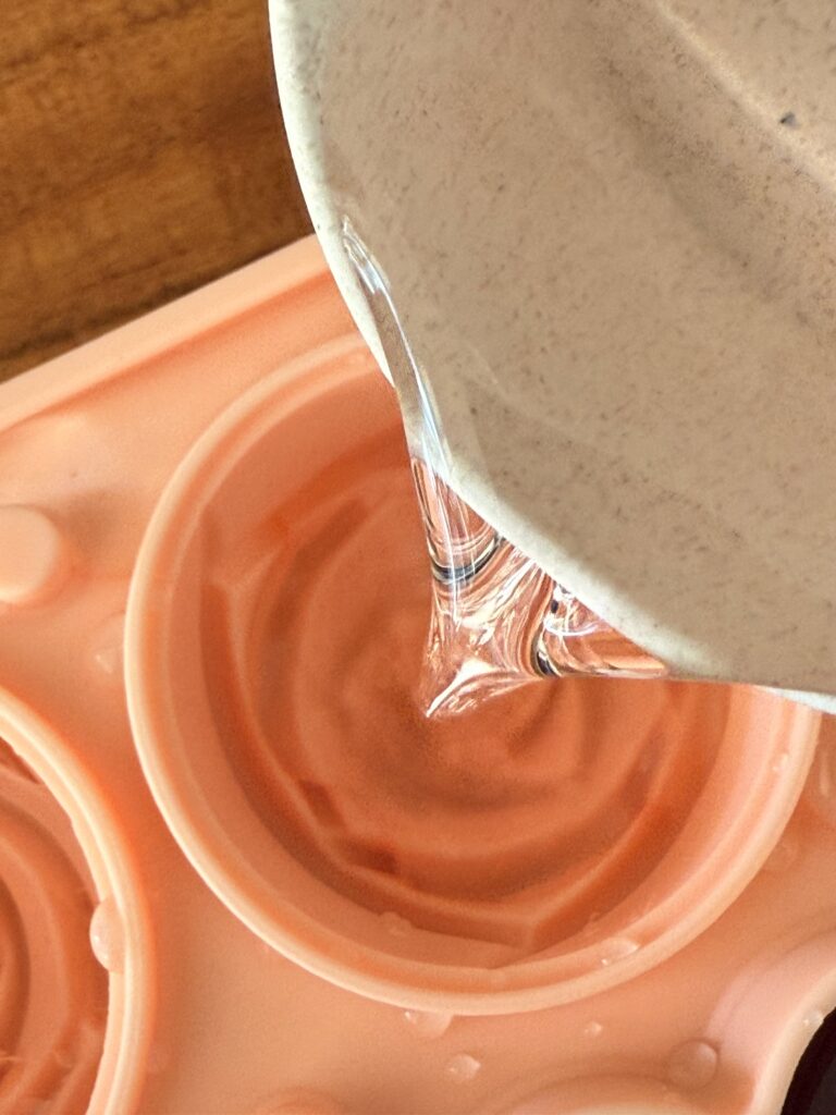 Pouring pink cranberry juice in a rose ice cube mold on the counter.