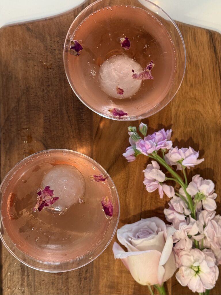 Ariel view of 2 coupe glassed with the rosette cocktail on a cutting board with roses and flowers on it.