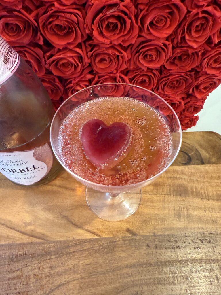 The Sweetheart cocktail on a brown cutting board on the counter surrounded by red roses.