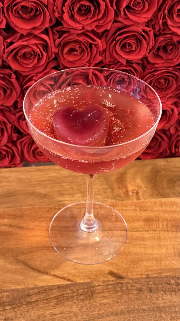 The Sweetheart cocktail on a brown cutting board on the counter surrounded by red roses.