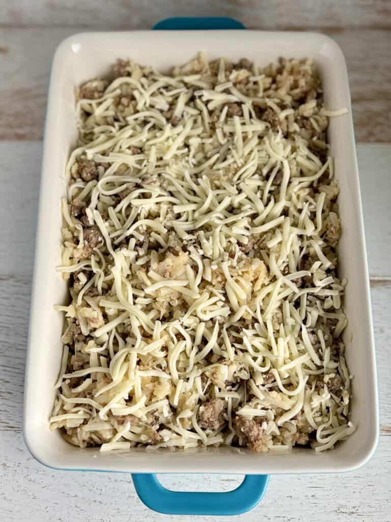 Baked sausage and potato casserole topped with shredded cheese in a white baking dish.