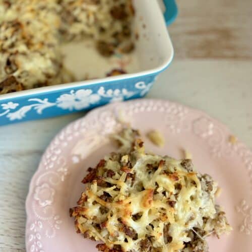 Close-up of a slice of sausage potato casserole on a pink plate, showing melted cheese, sausage, and crispy topping.