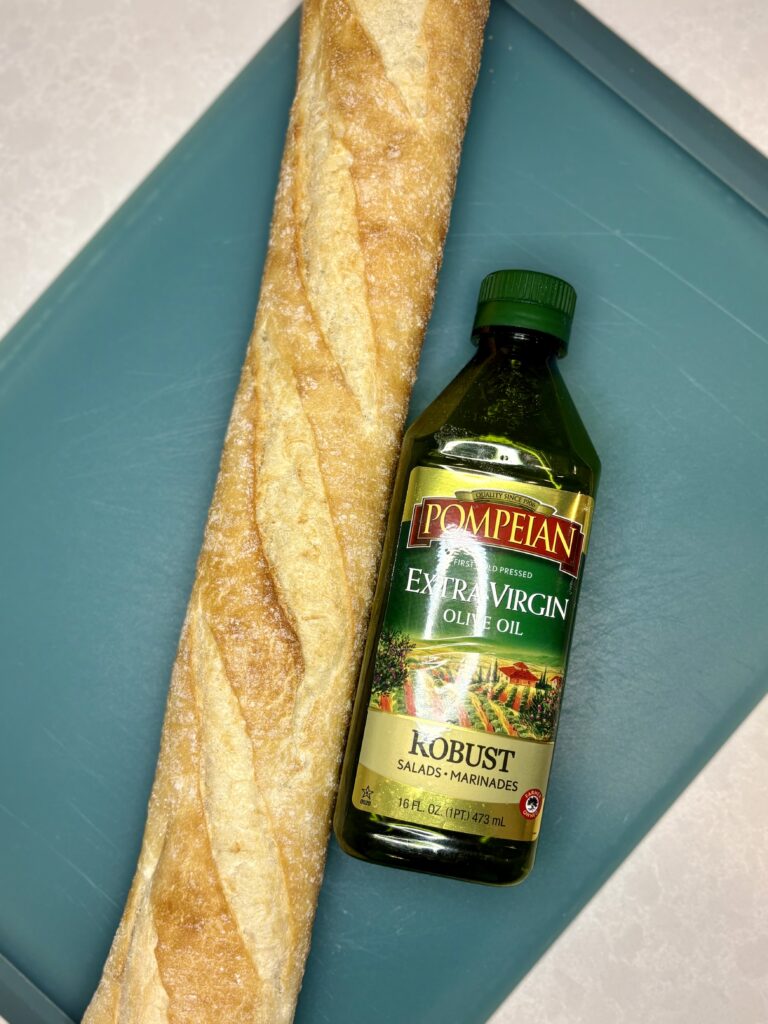 a baguette next to olive oil on a cutting board on a counter