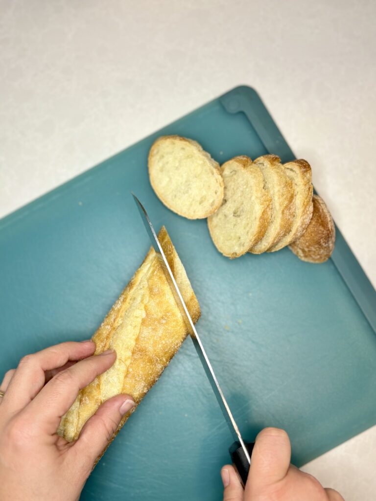 a baguette being sliced on a cutting board with a bread knife