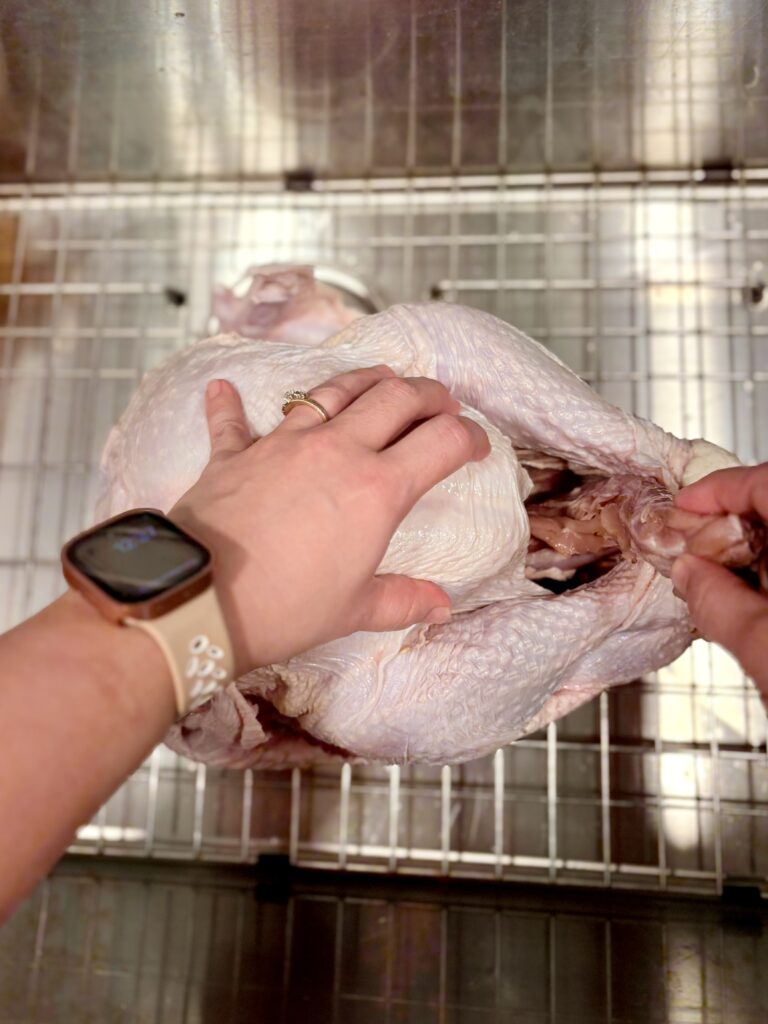 a raw turkey in a sink with the neck being removed from the cavity