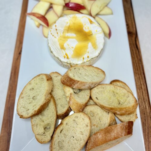 Baked brie on a plate with crostini and apple slices