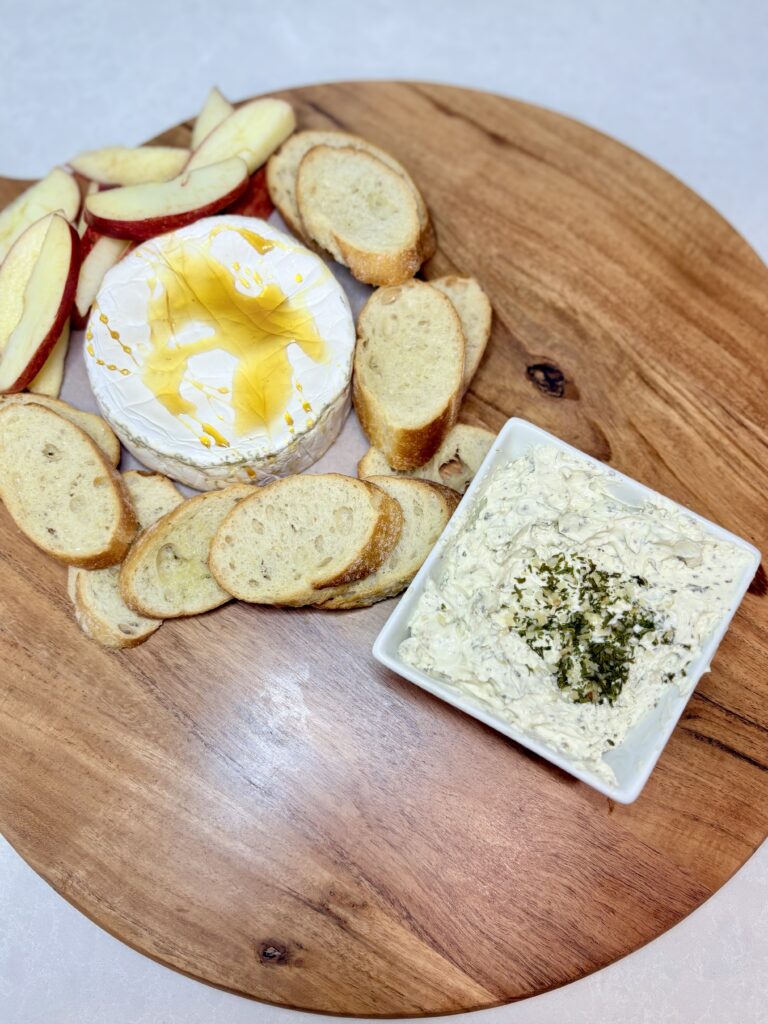 apple slices and crostini added around the brie on a board