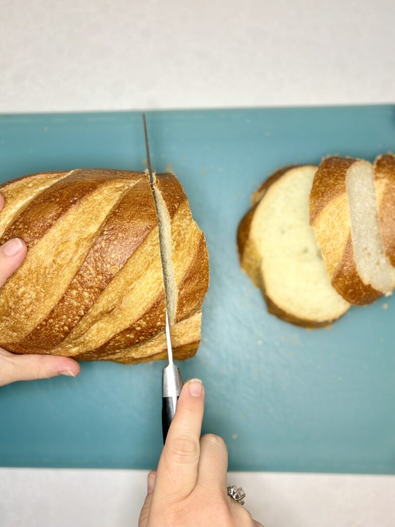 bread being sliced into 1 inch thick pieces on a cutting board 