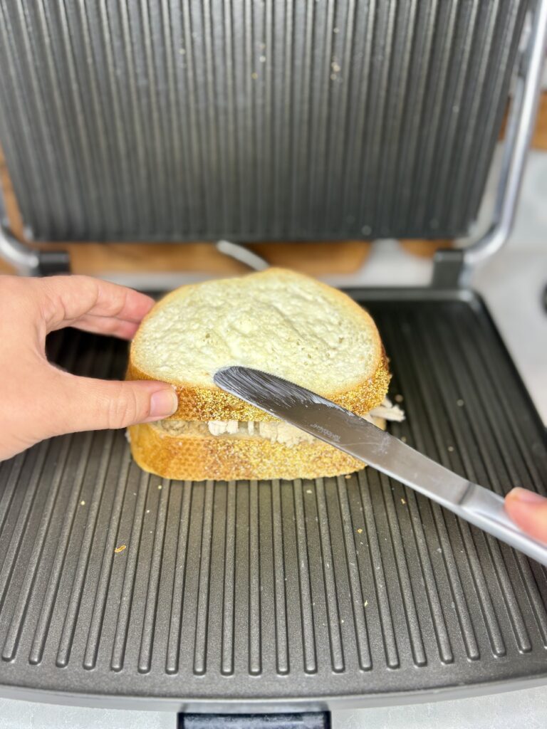 a buttered sandwich being place on a panini press 