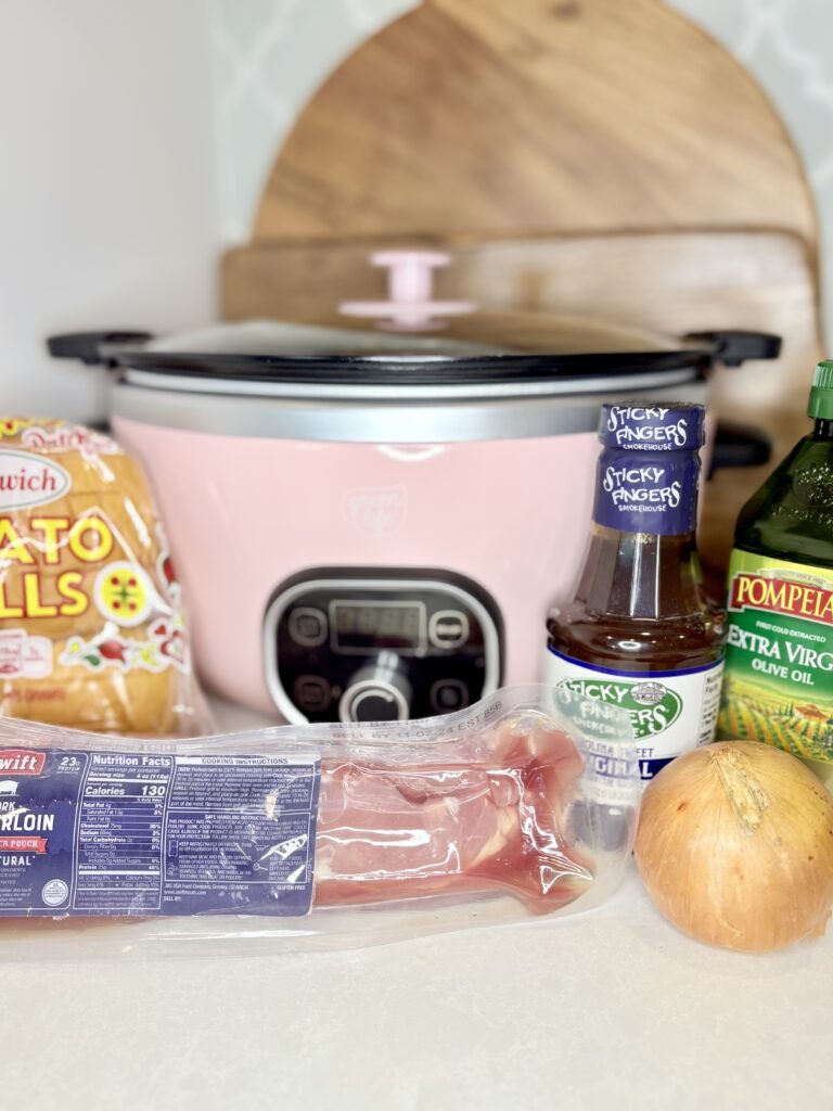 pork tenderloin, barbecue sauce, onion, olive oil and sandwich rolls on a counter with a slow cooker