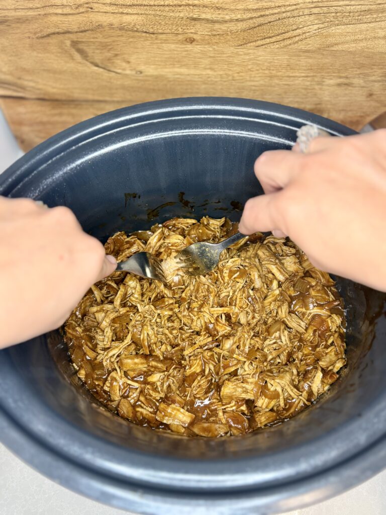 cooked pork tenderloin being shredded in a slow cooker with two forks