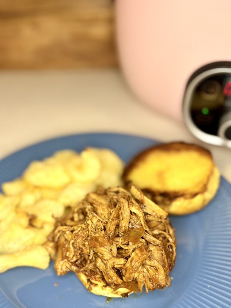 a plate with a pulled pork sandwich next to a pile of potato chips 