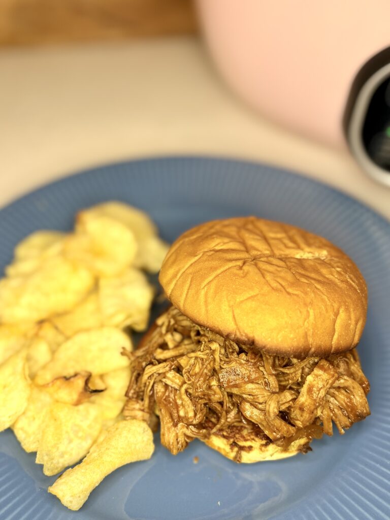 a pulled pork sandwich on a plate next to potato chips