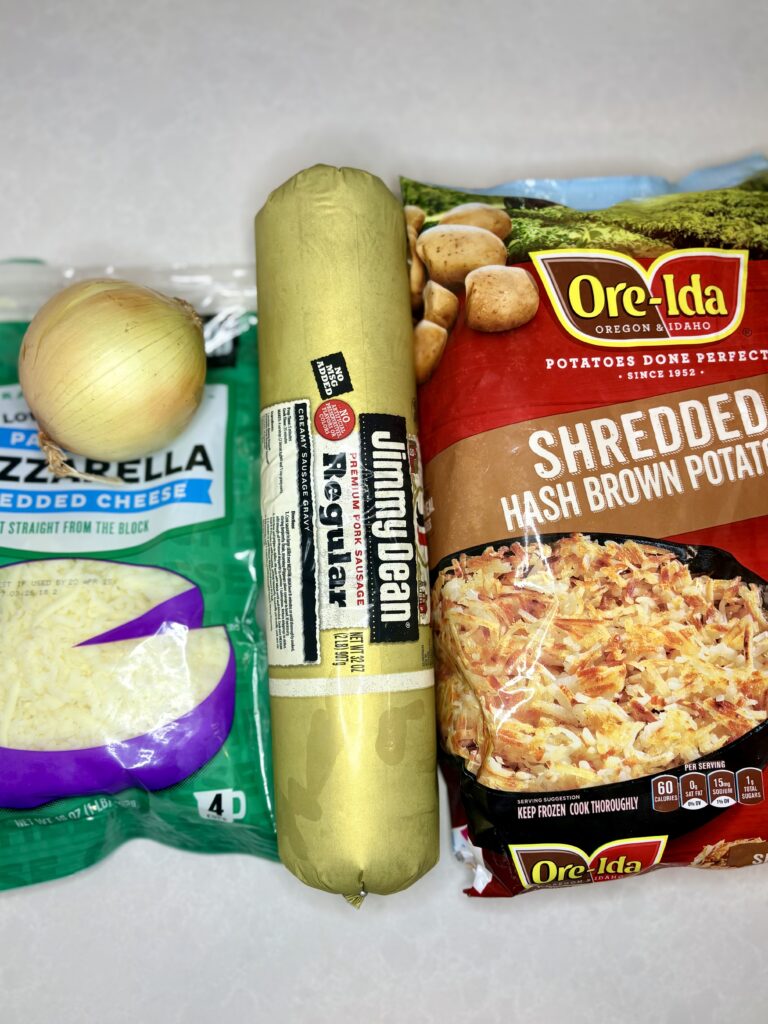 a bag of shredded mozzarella, on onion, a tube of pork sausage, and a bag of frozen shredded hash brown potatoes on a counter.