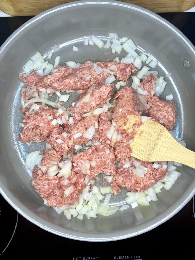 raw pork sausage and onion being browned in a pan on a stove