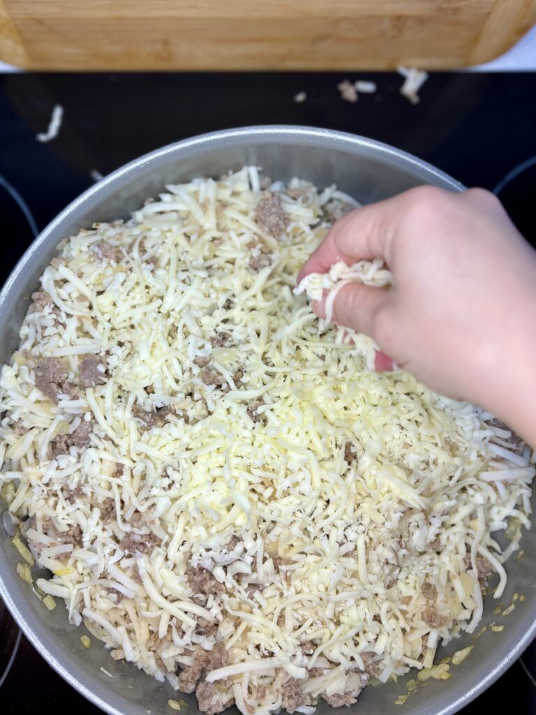 shredded mozzarella cheese being added to sausage potato mixture in pan