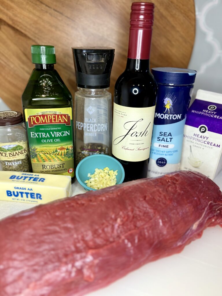 raw beef tenderloin, butter, thyme, red wine, olive oil, salt, pepper, red wine, garlic, and heavy cream on a counter