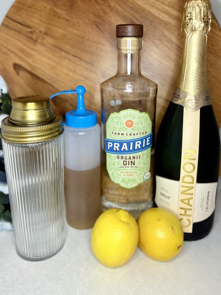 brut champagne, gin, simple syrup, and lemons next to a cocktail shaker on a counter