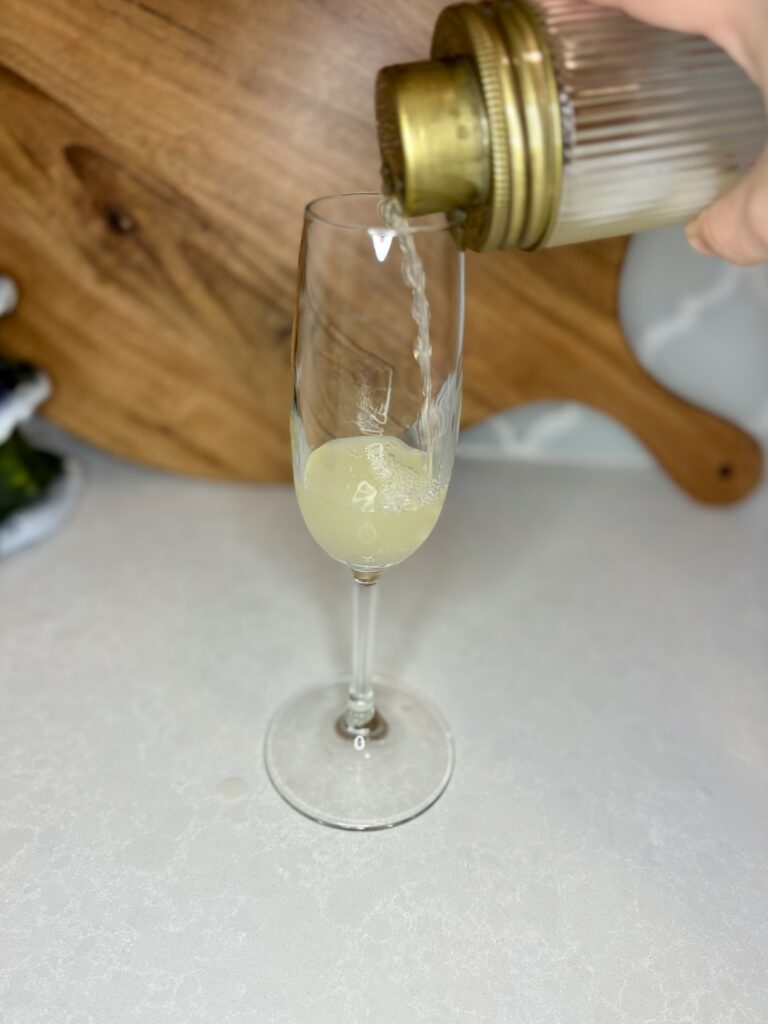 gin, lemon juice, and simple syrup being strained in to a champagne flute