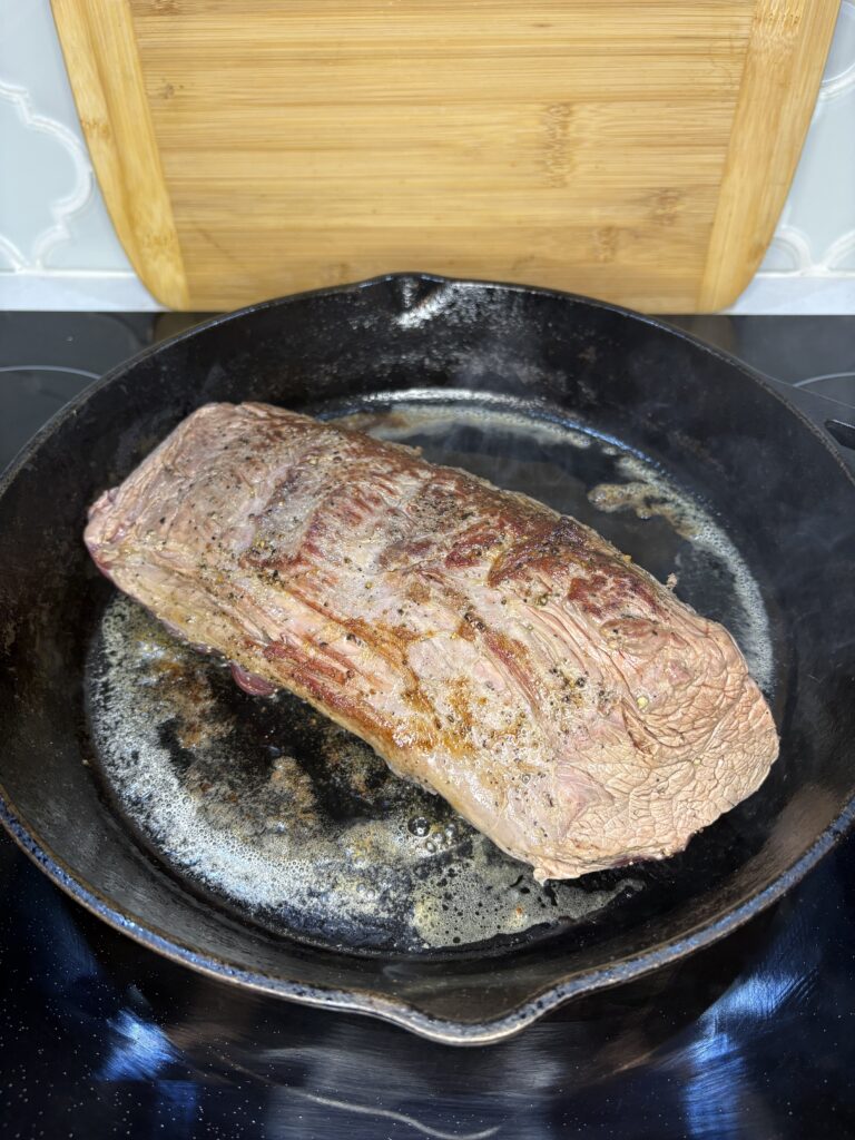 beef tenderloin searing in a cast iron skillet on a stove