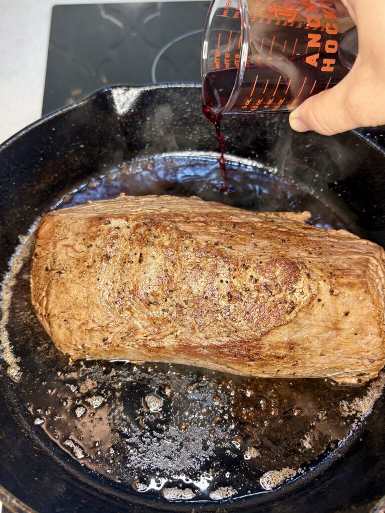 red wine being poured in to a skillet with beef tenderloin
