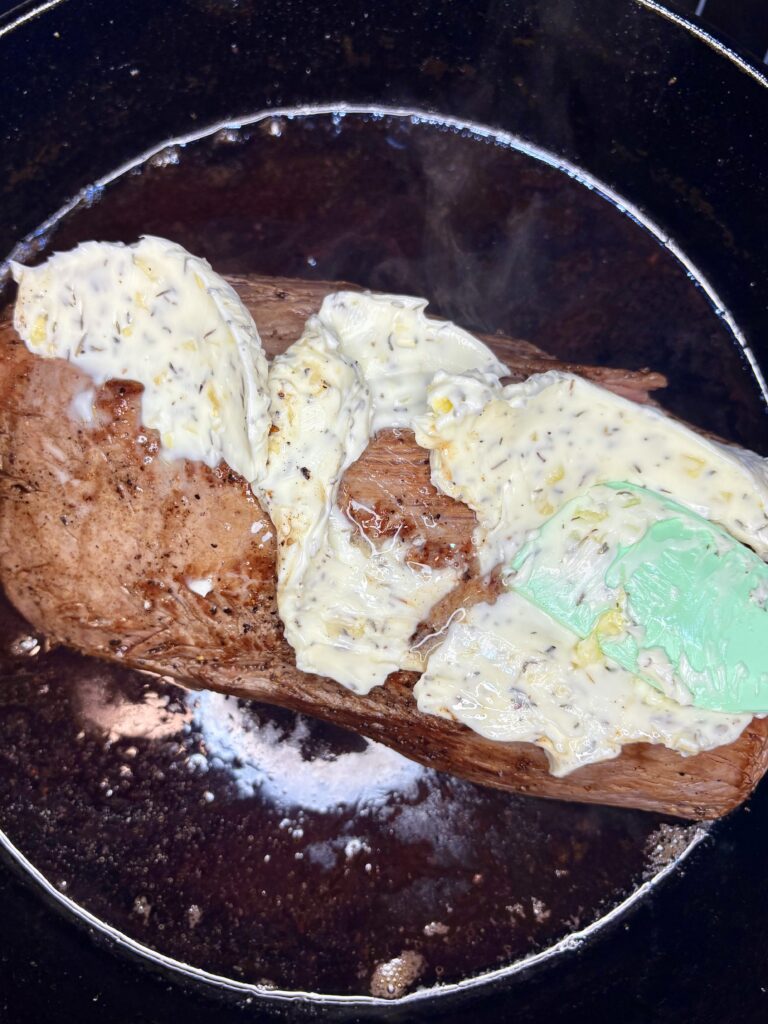 garlic butter being spread over beef tenderloin
