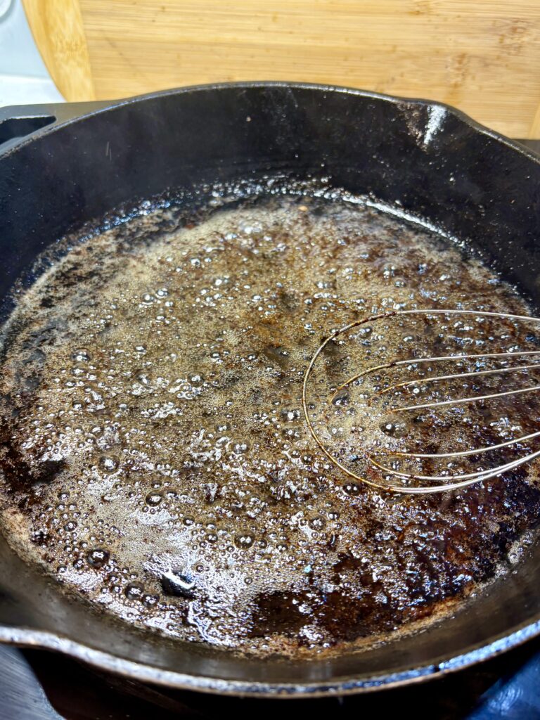 juice from cooked tenderloin in a skillet boiling on a stove being whisked